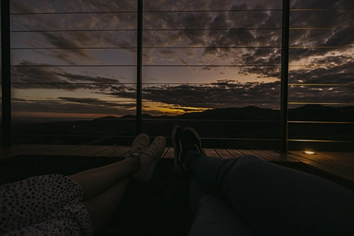 Casal relaxando no deck de madeira, contemplando um pôr do sol inesquecível nas montanhas