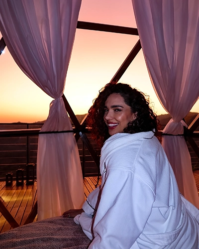 Hóspede relaxando na cama com o nosso roupão exclusivo, aproveitando o pôr do sol nas montanhas. Agradecemos por escolher o Domo Uaná.