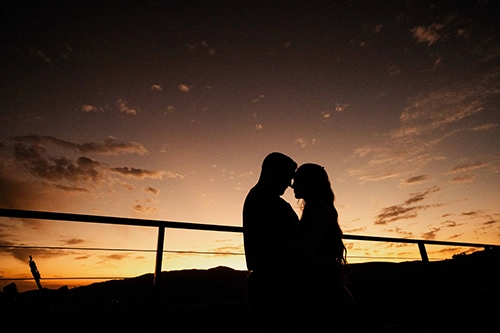 Silhueta de casal apaixonado no deck de madeira contemplando um pôr do sol inesquecível nas montanhas